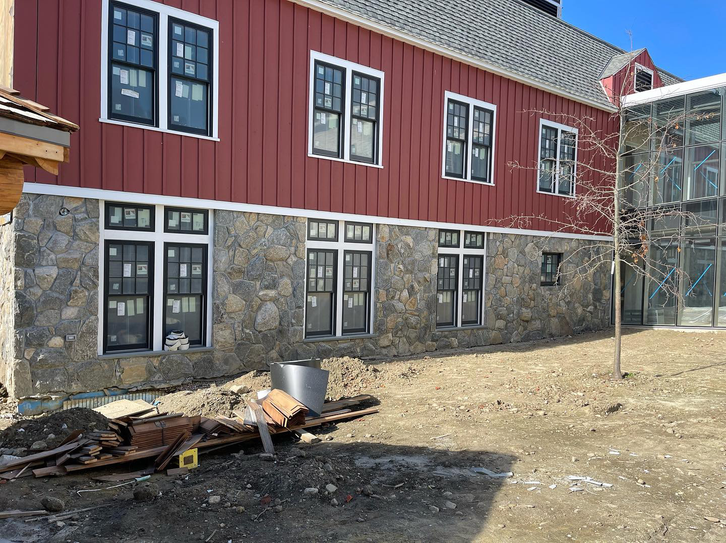 Long view of red barn with continuous fieldstone veneer along ground floor and glass atrium connector