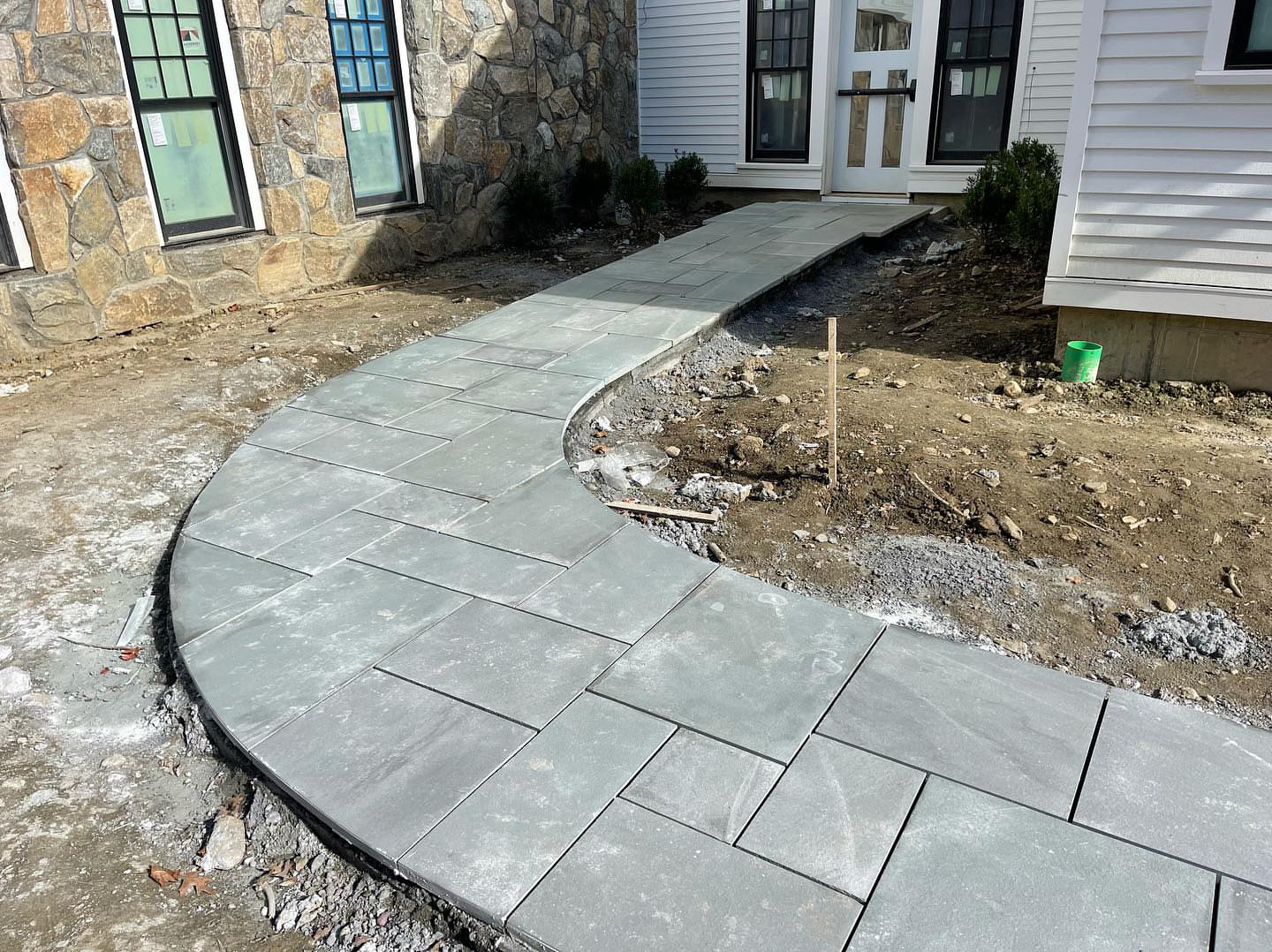 Curved bluestone paver walkway connecting stone-veneer lodge to white-sided building during construction