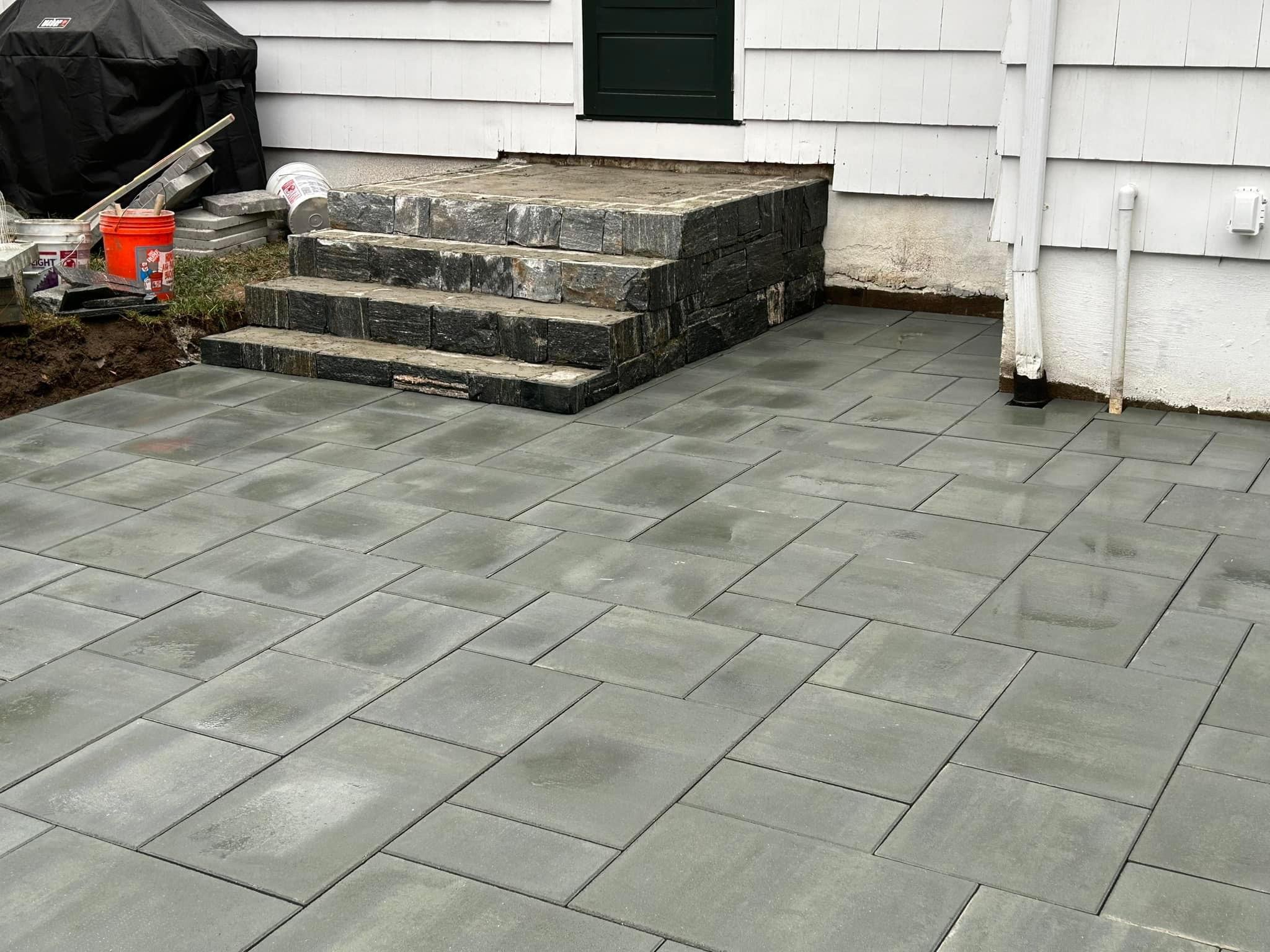 Close-up of paver patio with custom stone block steps leading to back door during construction