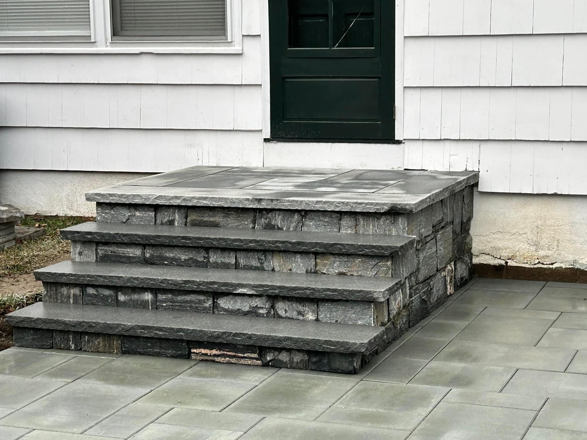 Close-up detail of custom three-tier stone block steps with paver treads and landing at back door