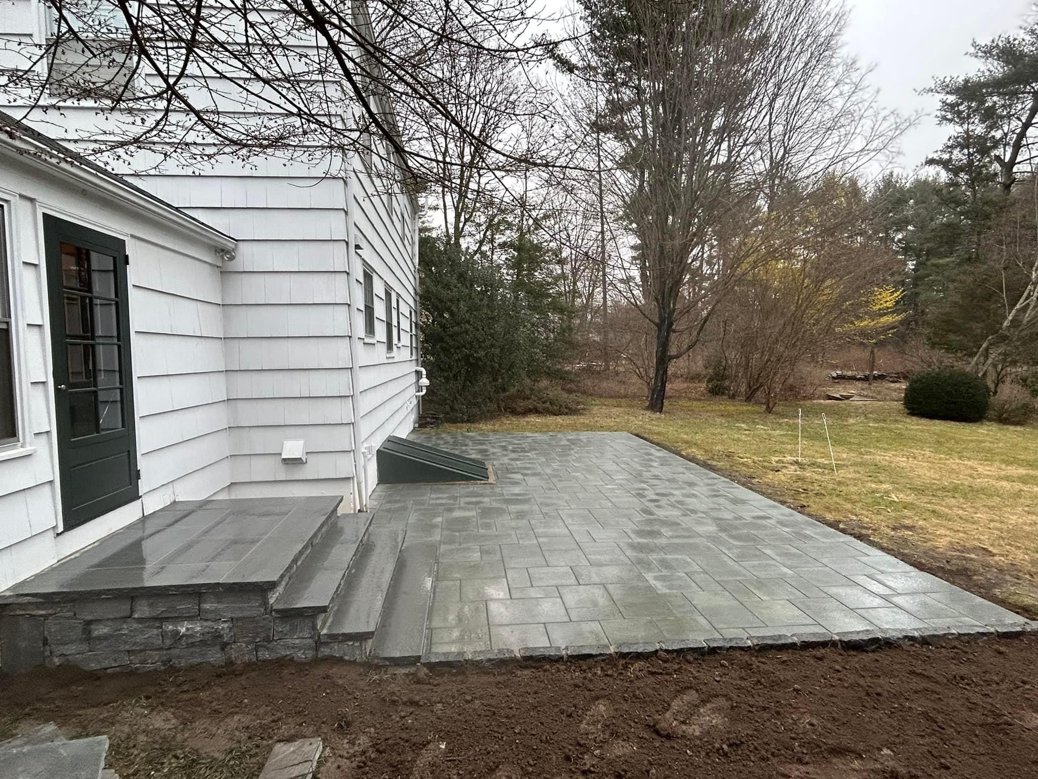 Completed paver patio with stone veneer steps at white colonial home, side angle showing clean finish