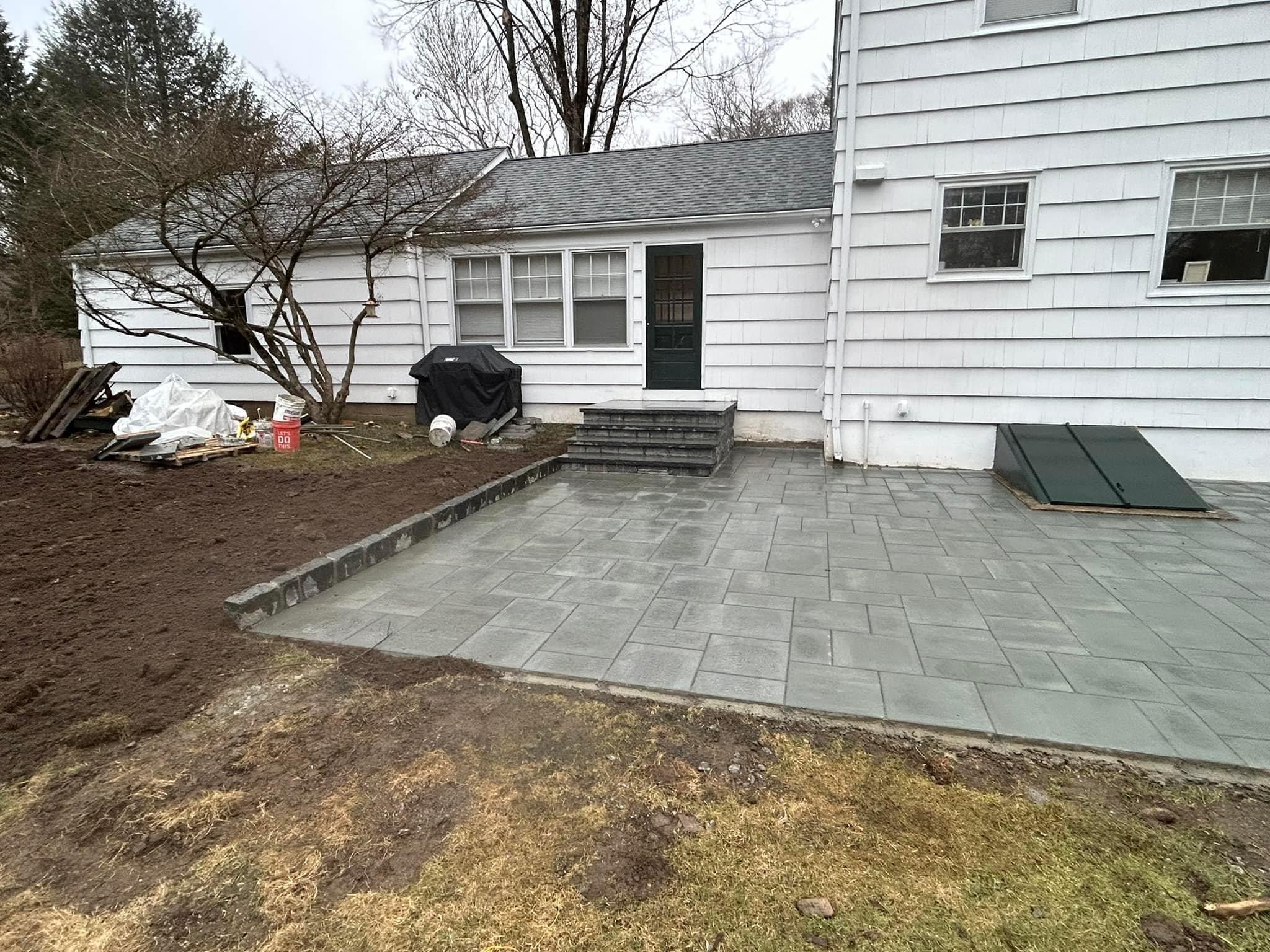 Completed paver patio with stone steps and cellar door at colonial home, fresh topsoil grading
