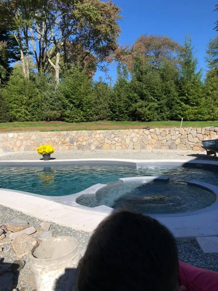 Freeform pool and spa with fieldstone retaining wall and landscaping on a sunny autumn day