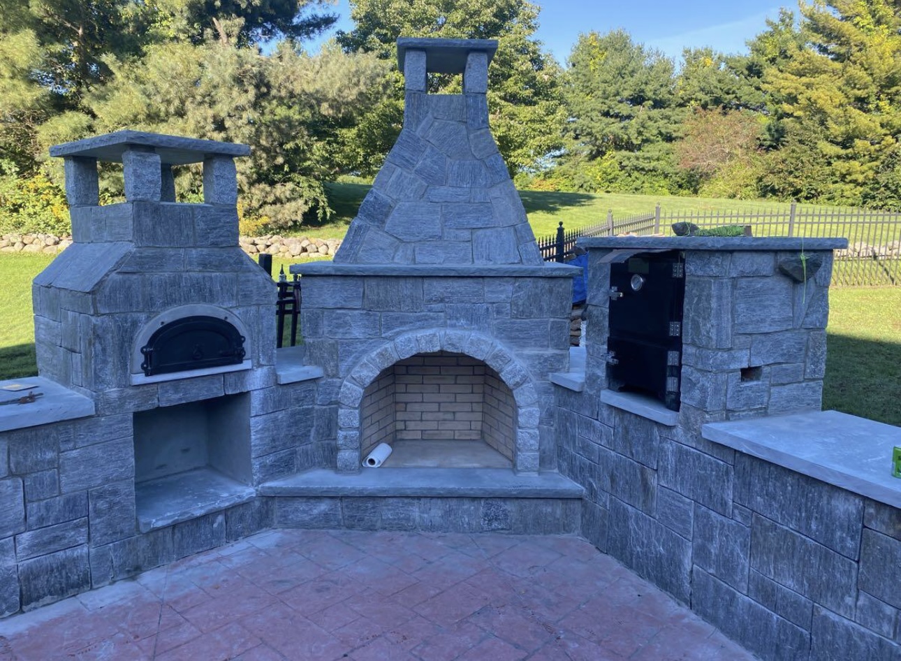 Grand outdoor fireplace complex with pizza oven, chimney, and storage built from cut stone