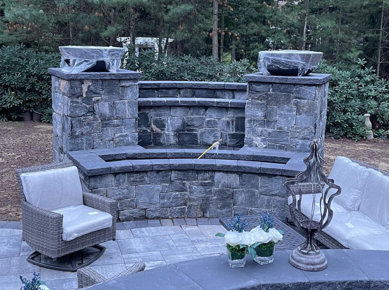 Close-up of stone seating wall with twin pillars, wicker furniture, and floral centerpiece