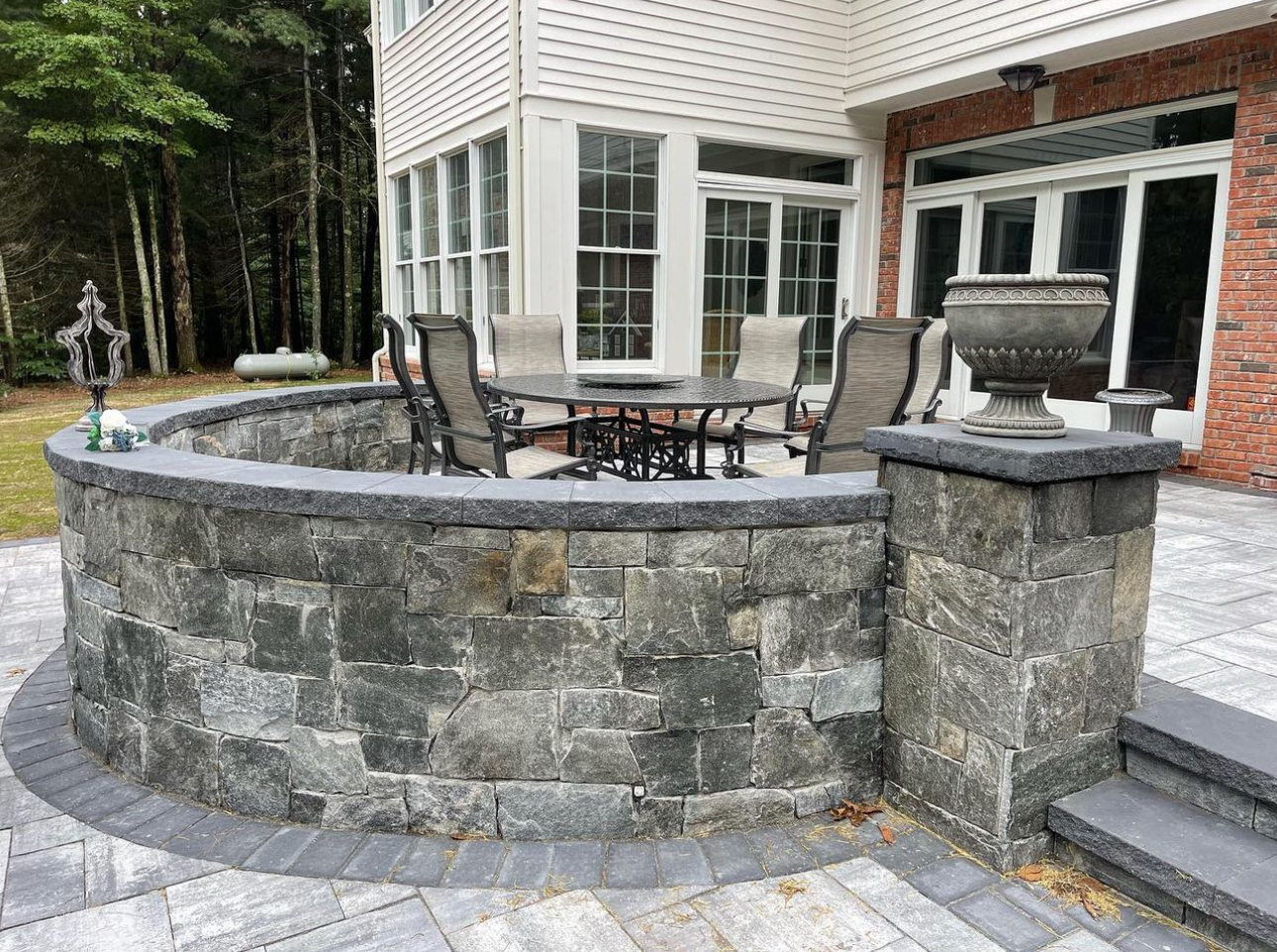 Curved stone seating wall with pillar caps, paver patio, and raised dining area