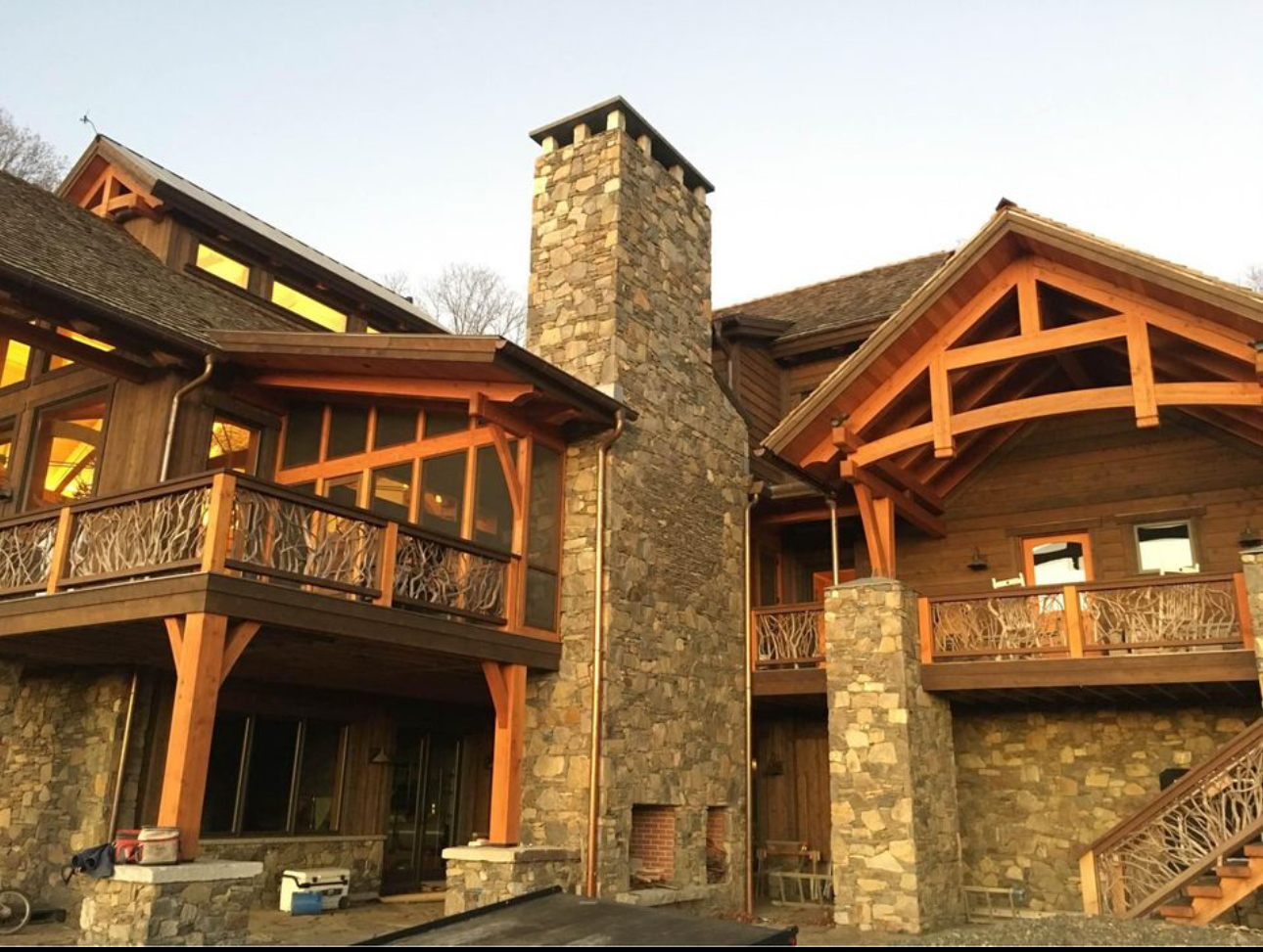 Towering fieldstone chimney on timber frame home with decorative branch railings