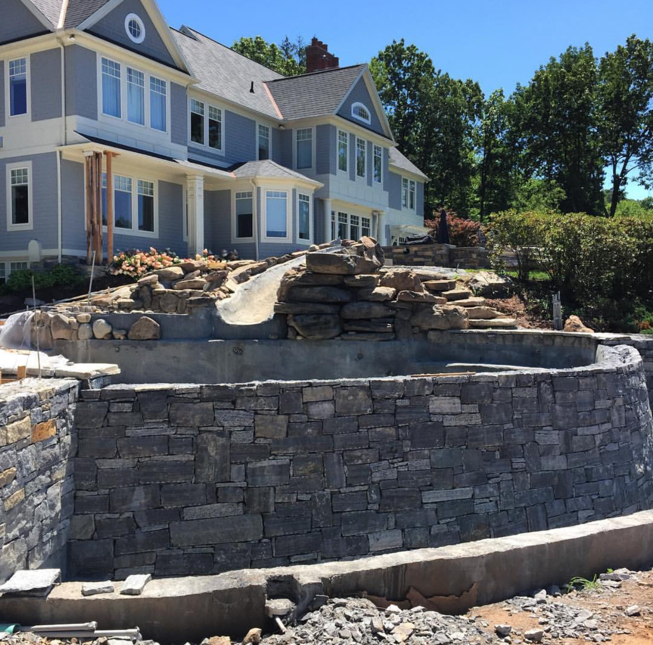 Large curved natural stone retaining wall under construction at a colonial home