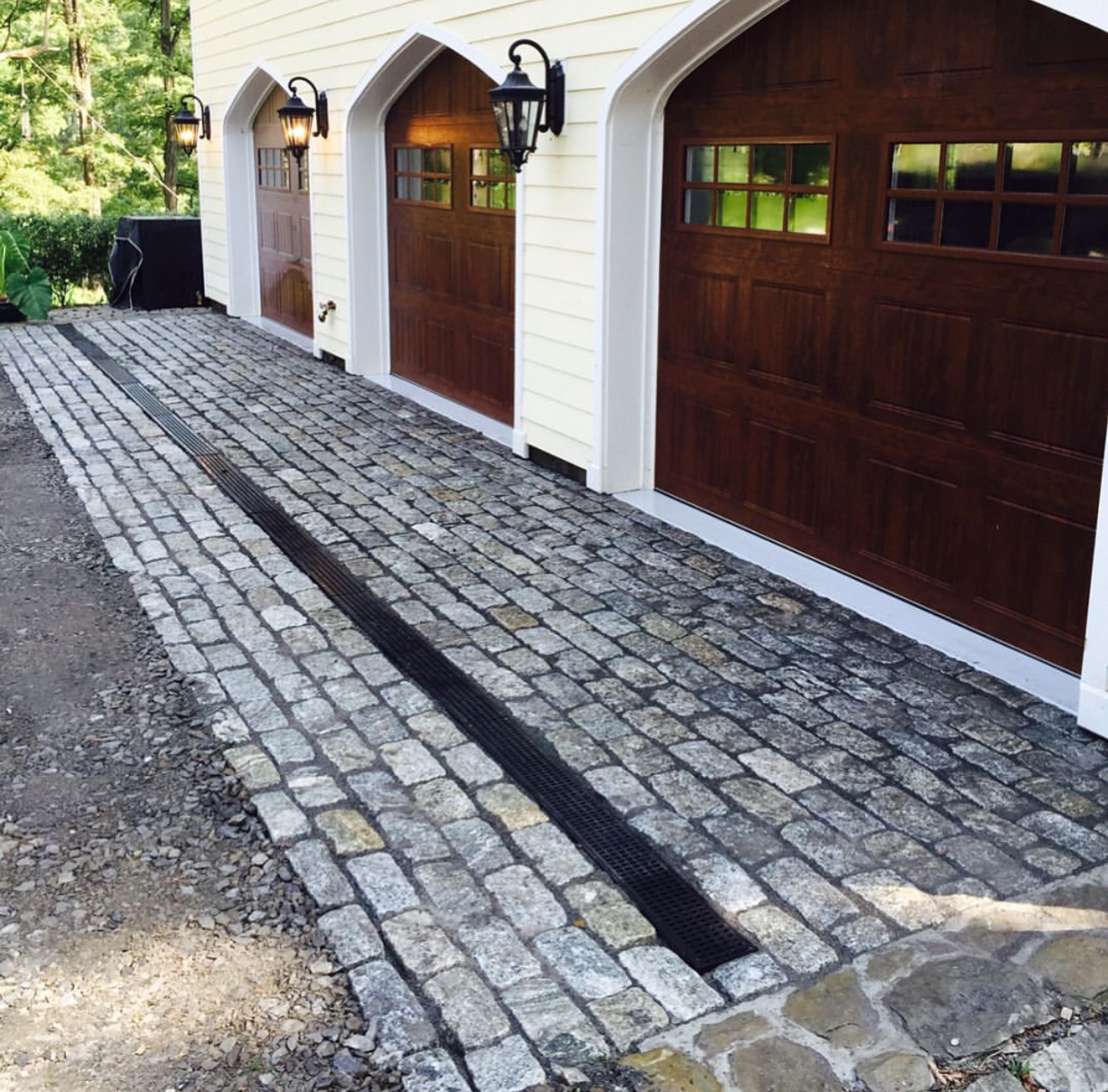 Cobblestone driveway with drainage channel in front of three-car garage with arched wood doors