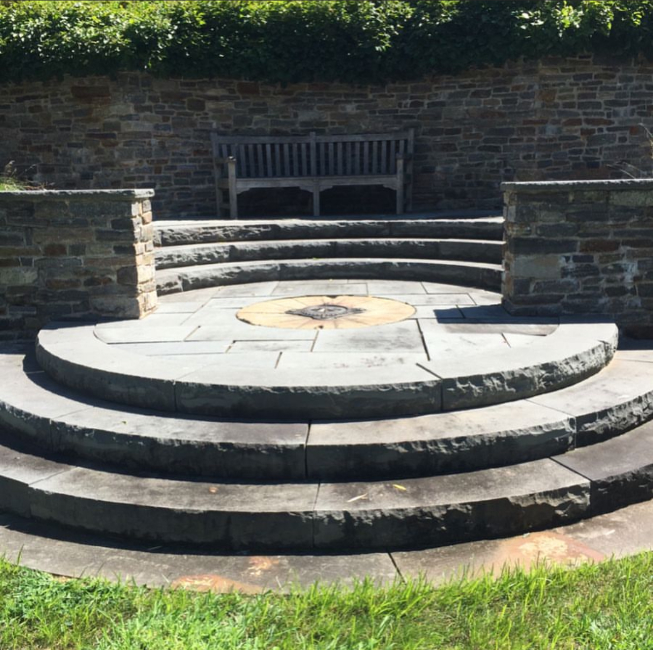 Circular tiered stone patio with compass rose inlay medallion and fieldstone retaining wall