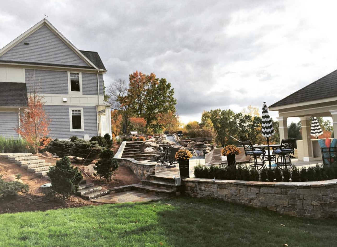 Multi-level backyard with stone retaining walls, steps, pool cabana, and autumn landscaping