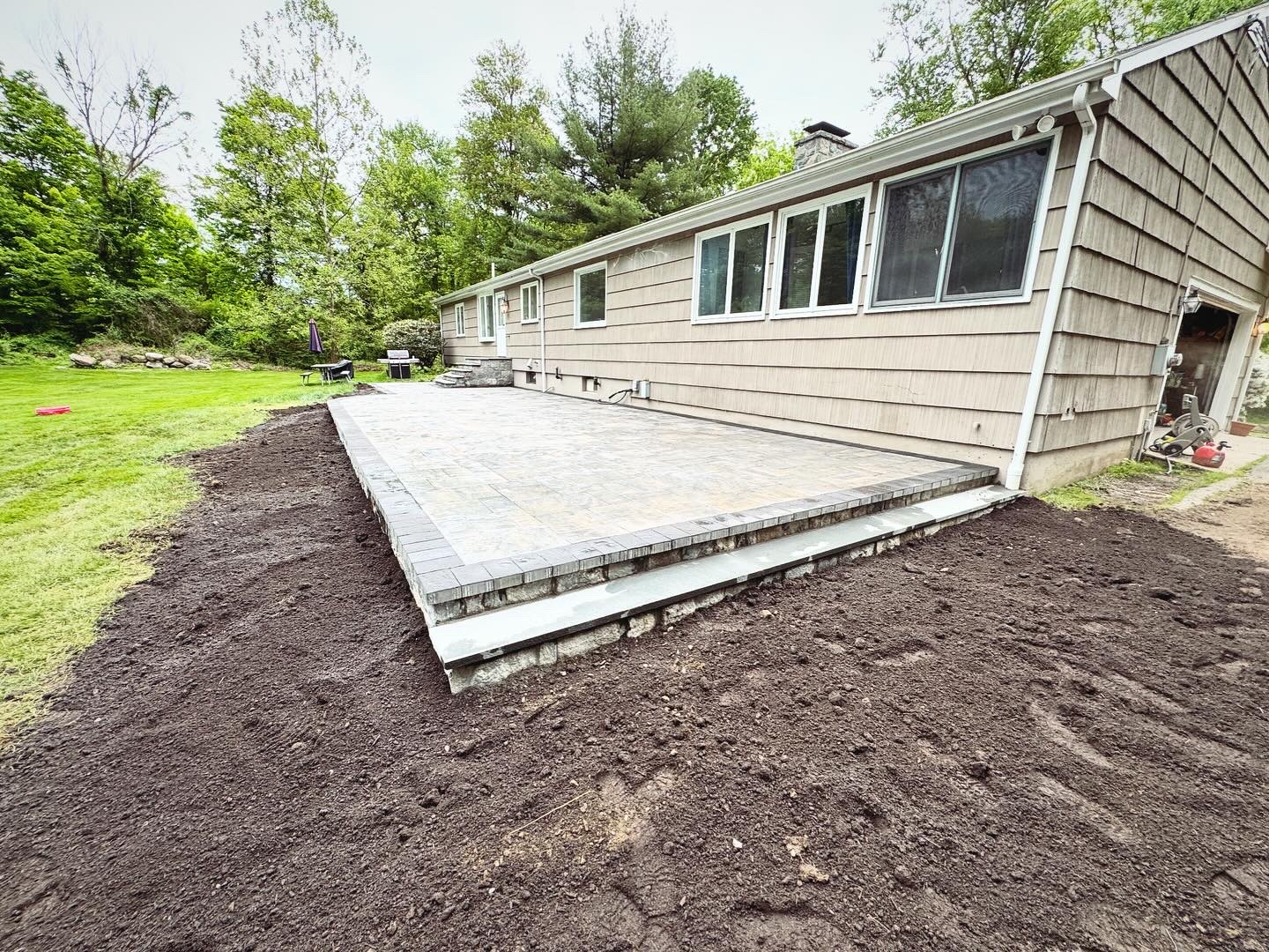 Completed raised paver patio with dark border, wide backyard view with fresh topsoil grading