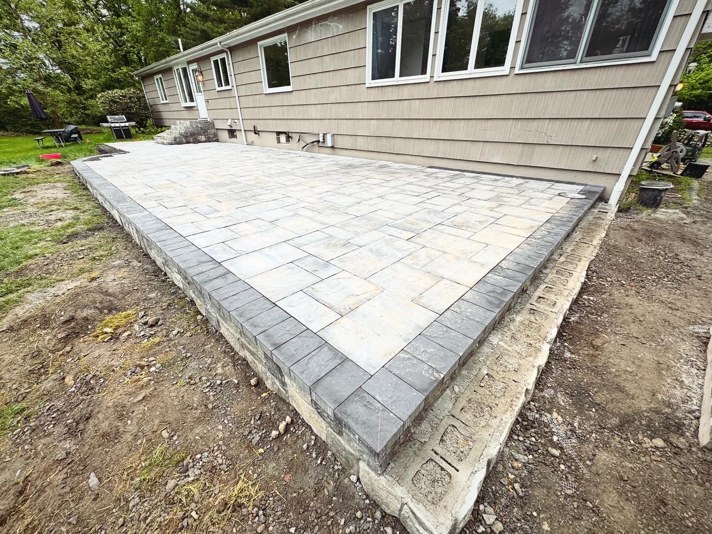 Raised paver patio with dark soldier course border and stone block edge, corner angle showing clean elevation