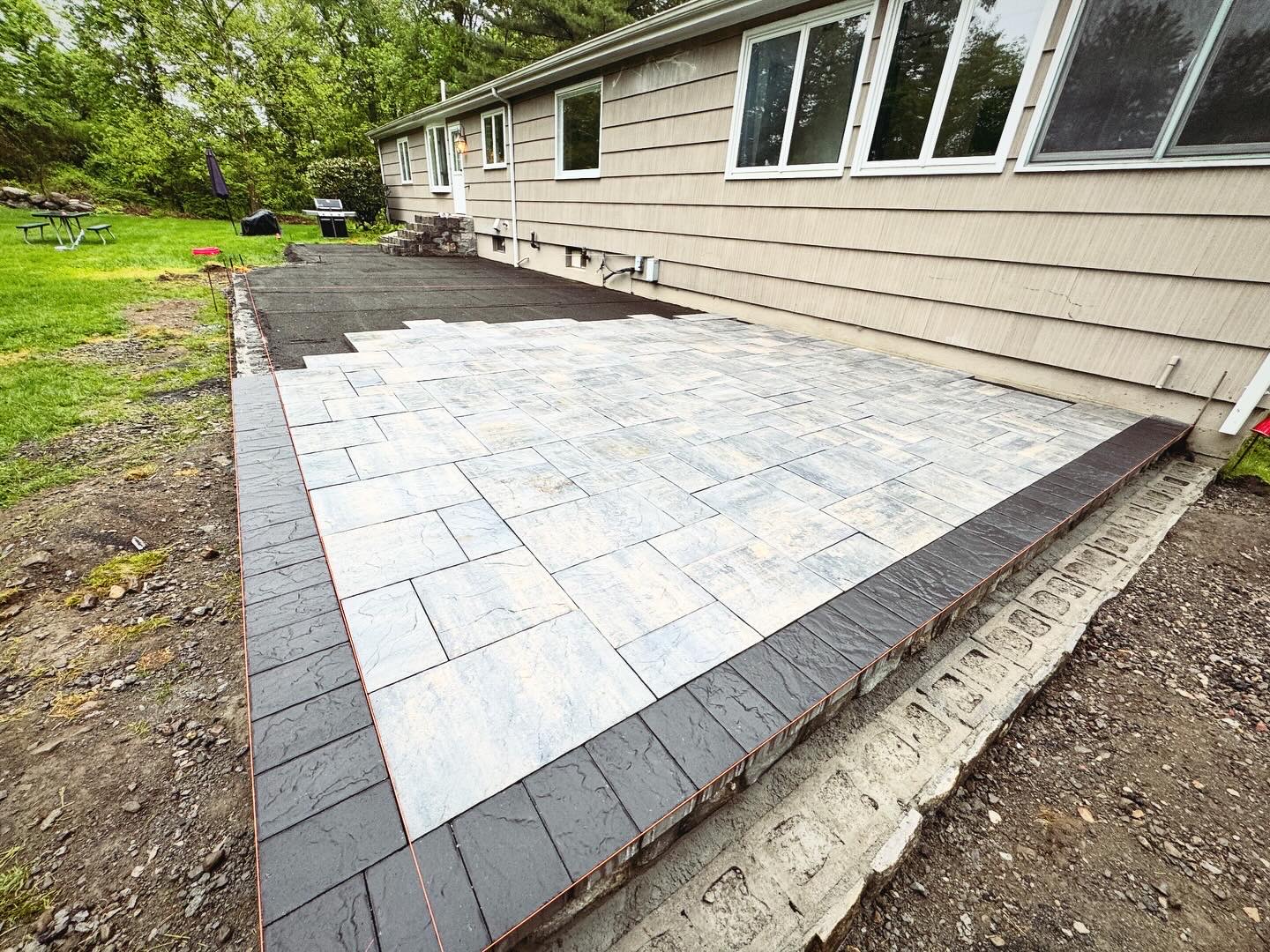 Two-tone paver patio with dark charcoal border in progress at a residential home