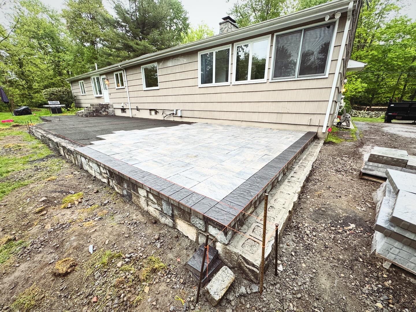 Raised paver patio with stone foundation wall and dark border pavers, residential home construction
