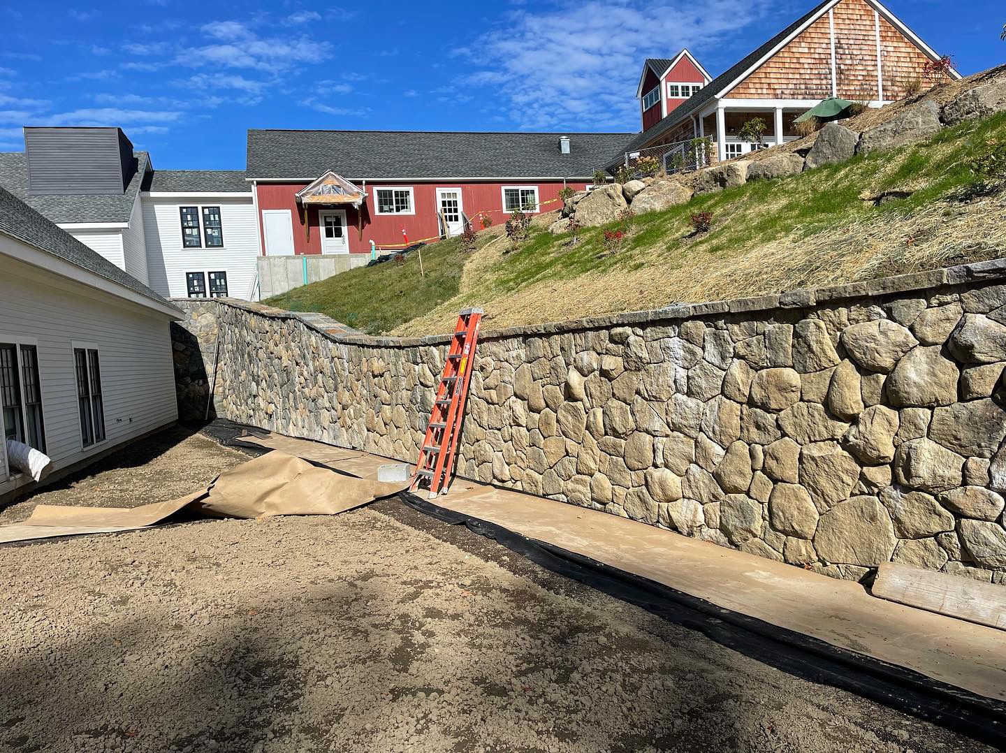 Large fieldstone retaining wall at commercial estate with red barn and cedar shingle buildings on hillside