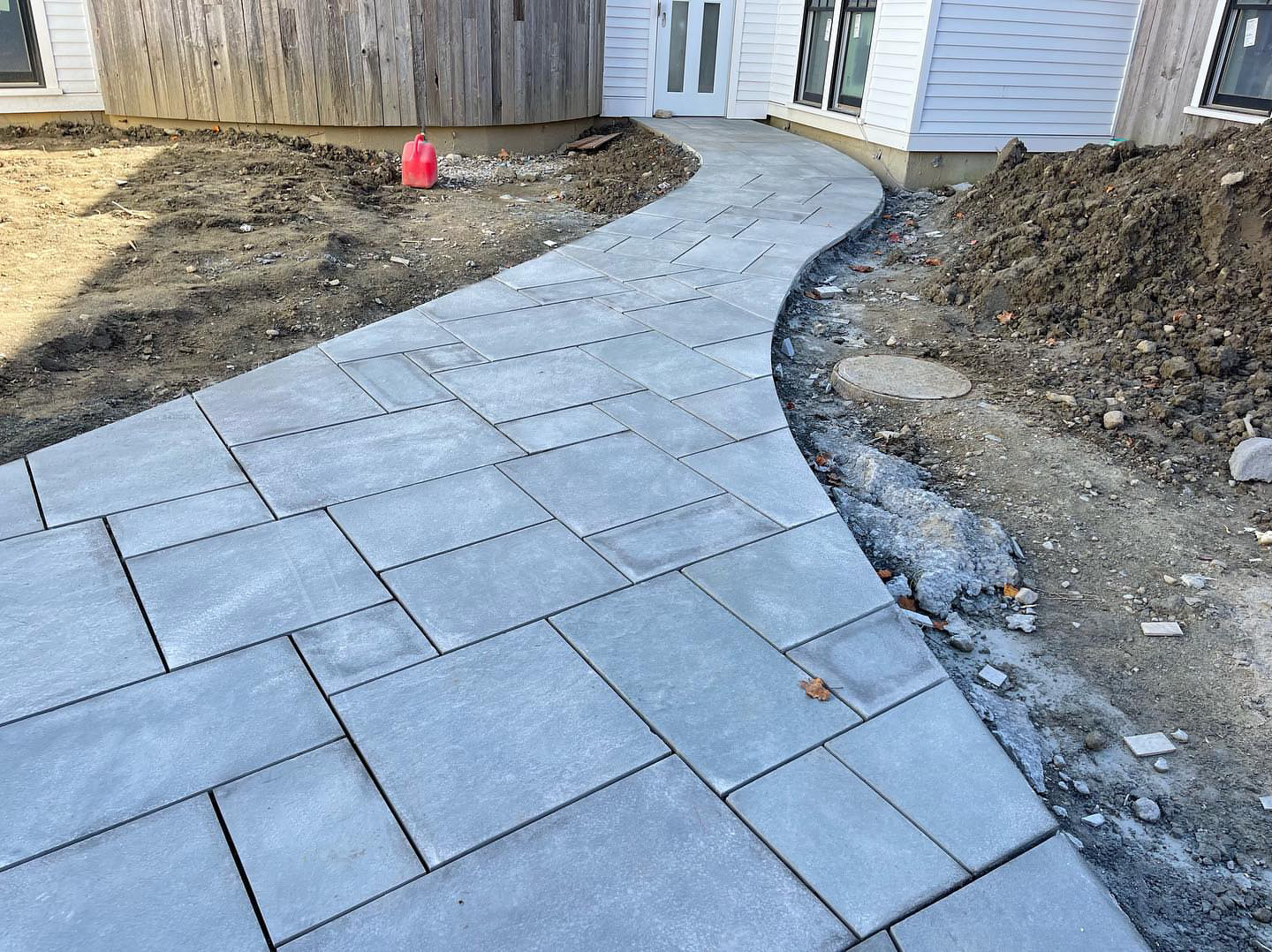 S-curved paver walkway between buildings under construction with drainage visible